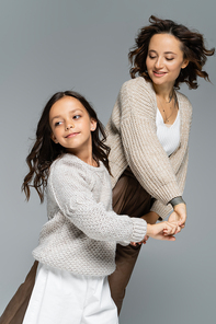 happy mother and daughter in autumn clothes holding hands while dancing isolated on grey
