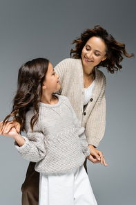 joyful mother and child looking at each other and holding hands while dancing isolated on grey