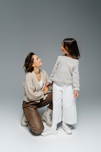 happy woman holding hand of stylish daughter on grey background