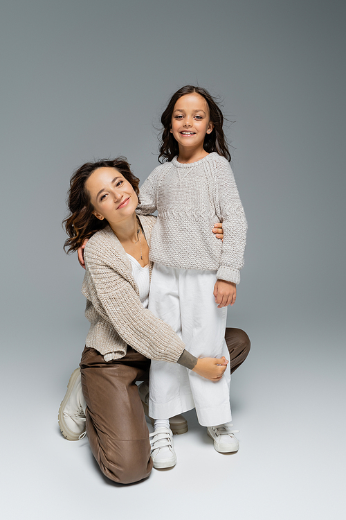 happy mother and child in stylish and warm clothes posing on grey background
