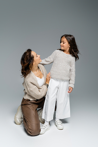 woman and girl in knitwear and trendy pants looking at each other on grey background