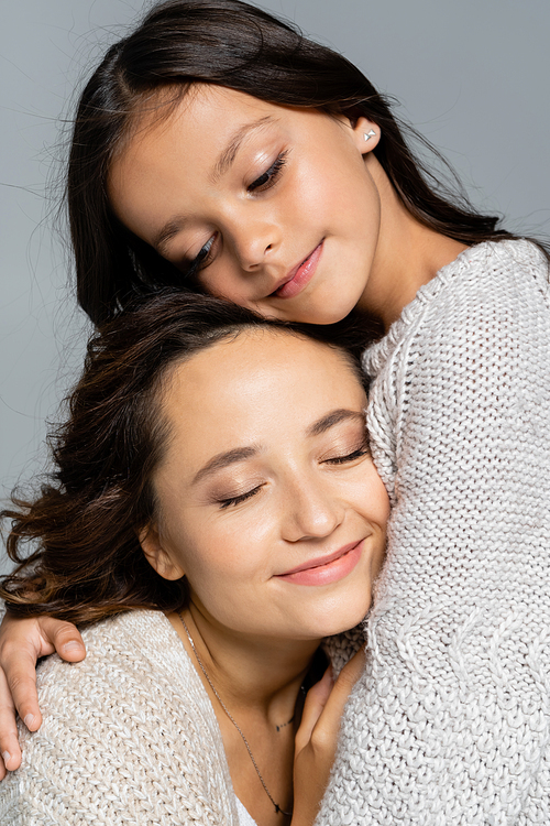brunette girl embracing mother smiling with closed eyes isolated on grey