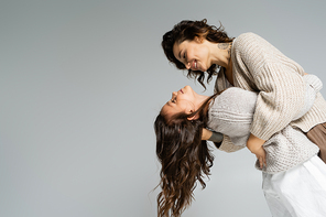 side view of smiling tattooed woman hugging daughter while dancing isolated on grey