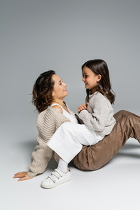 side view of happy mother and child in warm clothes looking at each other on grey background