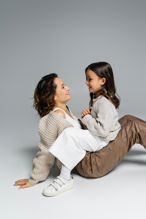 side view of happy mother and child in warm clothes looking at each other on grey background