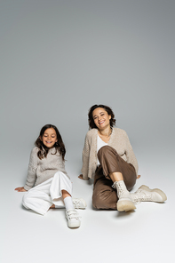 cheerful woman and child in trendy autumn outfit posing on grey background