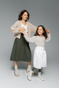 full length of woman and girl in skirts holding hands and dancing on grey background