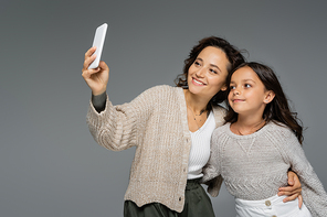 happy mother and daughter in warm knitted clothes taking selfie on smartphone isolated on grey