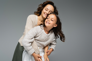 happy woman with closed eyes hugging daughter in warm knitwear isolated on grey