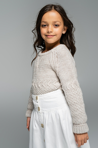 brunette child in cozy autumn sweater smiling at camera isolated on grey
