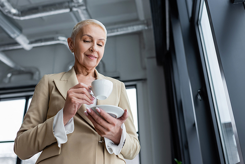 low angle view of positive senior businesswoman holding coffee cup in office