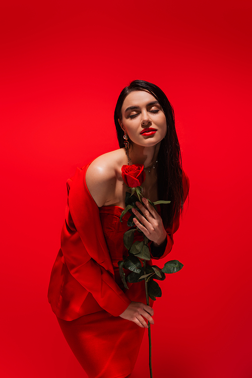 Elegant woman in jacket posing with rose flower isolated on red