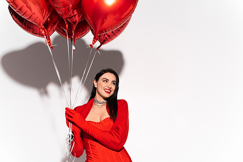 Smiling woman with red lips holding heart shaped balloons on white background