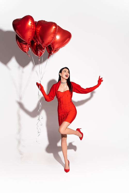Excited woman in dress and heels holding red heart shaped balloons on white background with shadow
