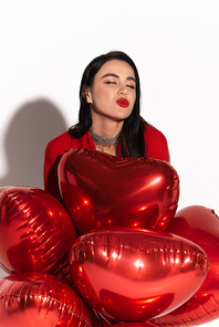 Stylish woman with red lips blowing kiss near heart shaped balloons on white background with shadow