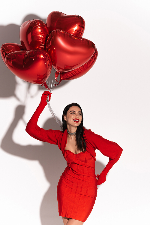 Trendy woman in red dress holding heart shaped balloons on white background with shadow