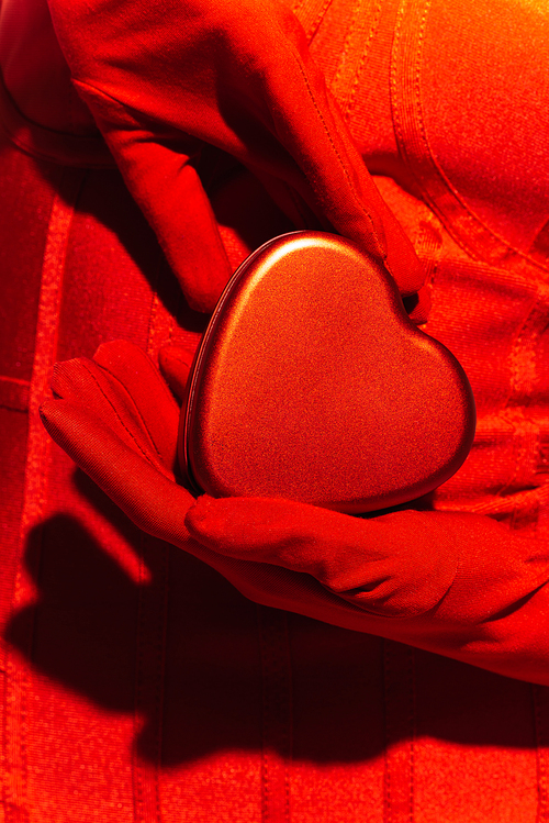 Cropped view of woman in red dress and gloves holding gift box in heart shape