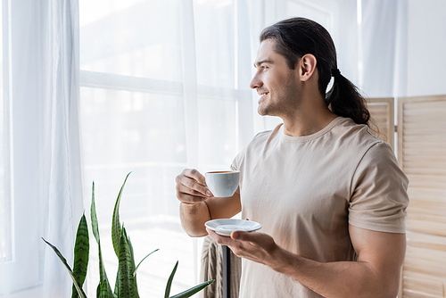 happy man with long hair holding cup of coffee and saucer