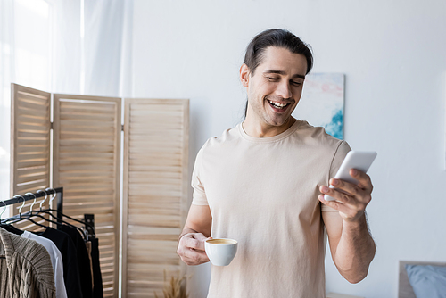 happy man in t-shirt holding cup of coffee and using smartphone
