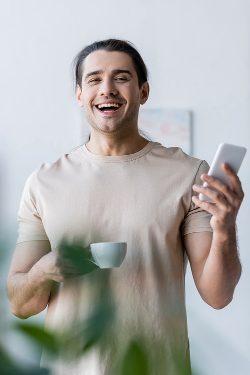 happy man in t-shirt holding cup of coffee and smartphone