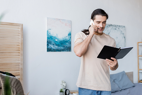 man talking on mobile phone and holding notebook at home