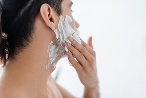shirtless man applying shaving foam on face in bathroom
