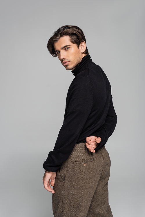 good looking man in black turtleneck and pants looking at camera isolated on grey