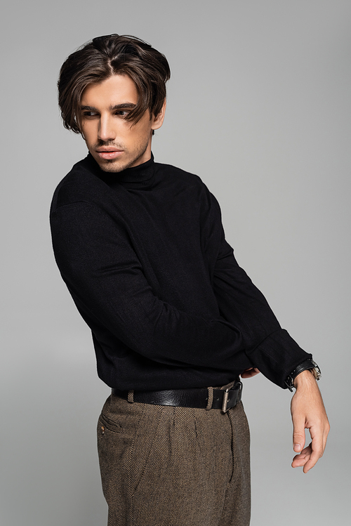 brunette young man in black turtleneck posing and looking away isolated on grey