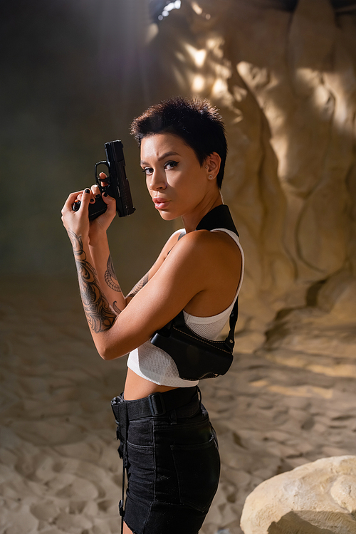 brunette archaeologist with holster holding gun and looking at camera in desert