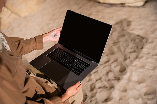 cropped view of archaeologist with tattoo using laptop in cave during expedition