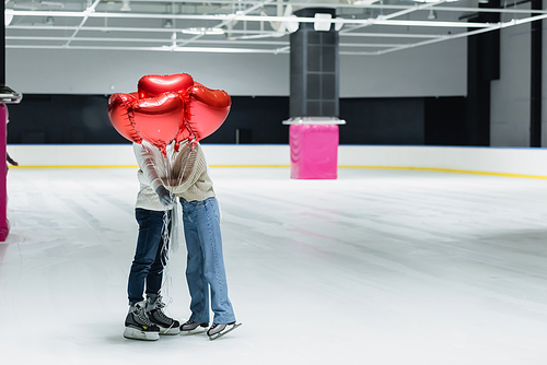 Couple hugging and holding red balloons in shape of heart on ice rink