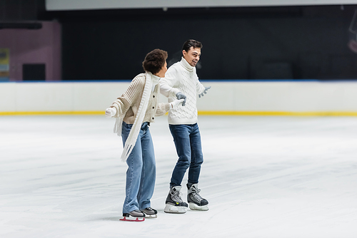 Positive multiethnic couple having fun while ice skating on rink