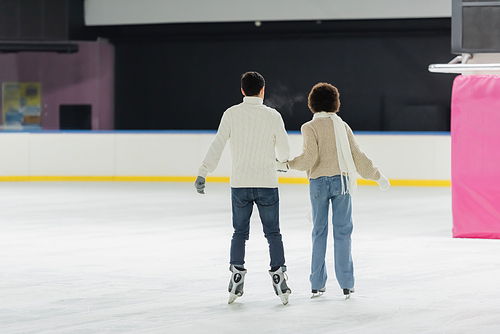 Back view of interracial couple ice skating together on rink