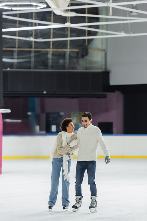 Smiling african american woman hugging boyfriend in sweater on ice rink