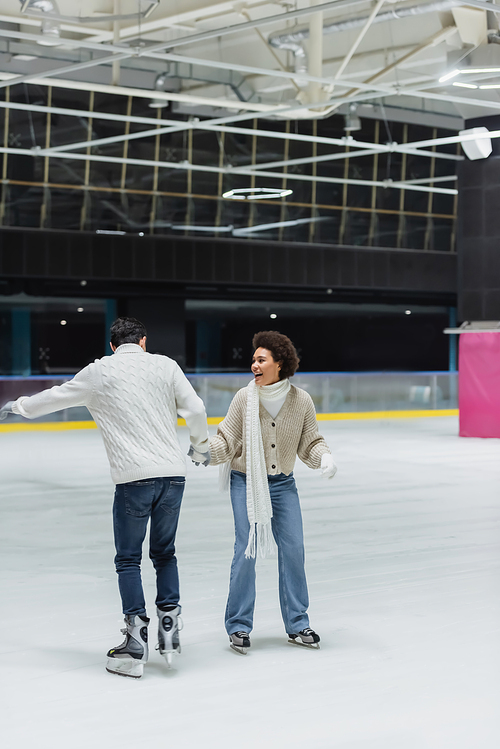 Happy african american woman ice skating with boyfriend on rink