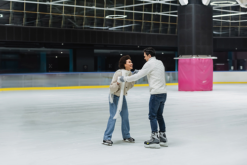 Cheerful african american woman holding hands of boyfriend while having fun on ice rink