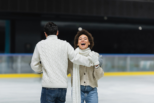 African american woman laughing while ice skating with boyfriend on ice rink