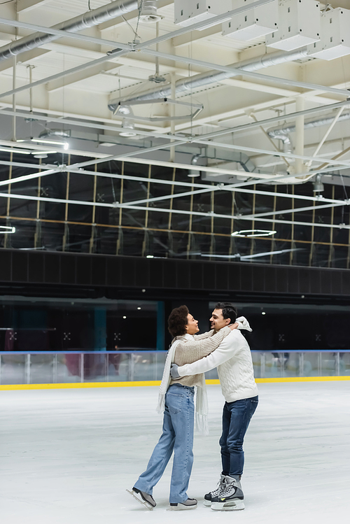 Side view of cheerful african american woman embracing boyfriend on ice rink