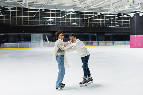 Positive multiethnic couple in gloves looking at camera while having fun on ice rink