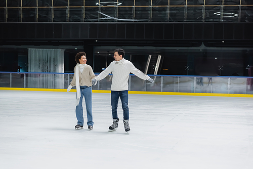 Positive interracial couple ice skating during date on rink