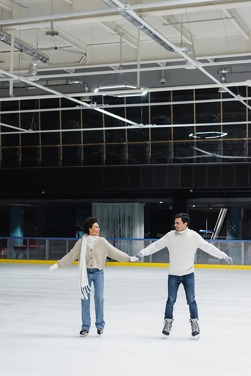 Smiling young interracial couple ice skating and holding hands on rink