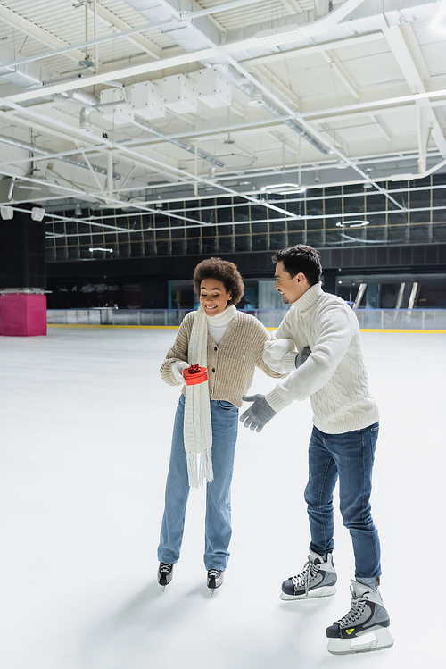 Excited african american woman holding heart shaped box near boyfriend on ice rink