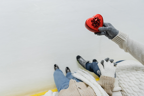 Top view of man holding hand of girlfriend and heart shaped gift box on ice rink