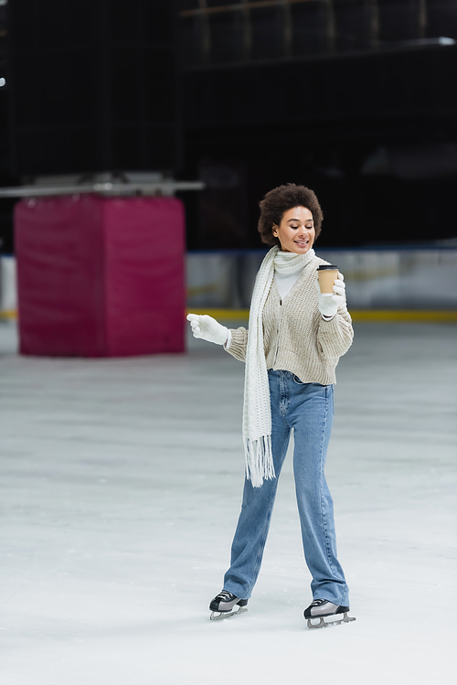 African american woman ice skating and looking at coffee to go on rink