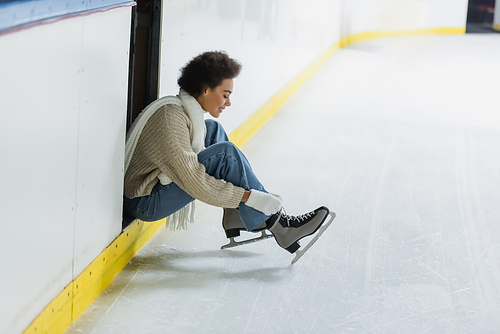 Side view of smiling african american woman wearing ice skates on rink