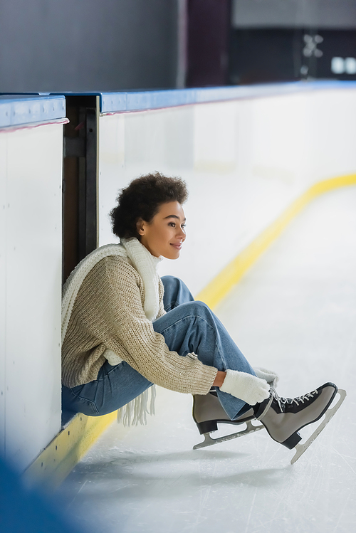 Positive african american woman wearing ice skates and looking away on rink