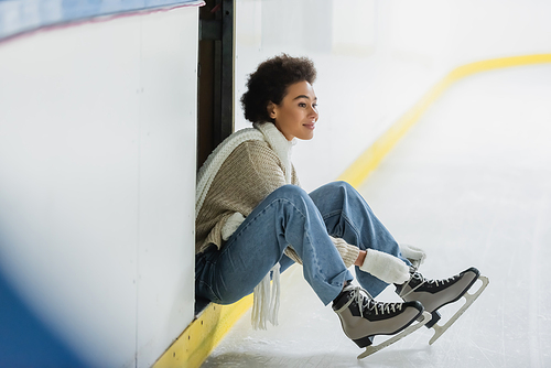 Happy african american woman wearing ice skates on blurred rink