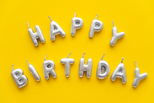Top view of festive candles in shape of Happy Birthday lettering on yellow background
