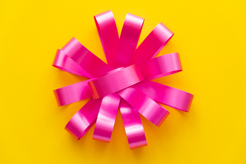 Top view of pink gift bow on yellow background