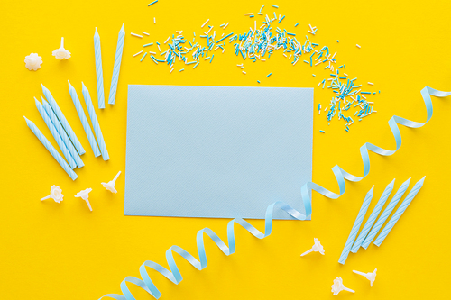 Top view of empty greeting card near candles and blue serpentine on yellow background
